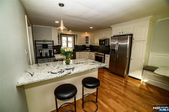 kitchen with a peninsula, a breakfast bar, dark wood-style flooring, appliances with stainless steel finishes, and glass insert cabinets