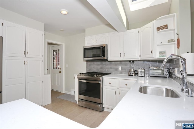 kitchen featuring white cabinets, decorative backsplash, appliances with stainless steel finishes, open shelves, and a sink