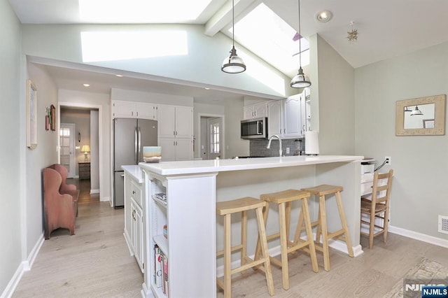 kitchen featuring stainless steel appliances, a breakfast bar, a peninsula, white cabinets, and decorative backsplash