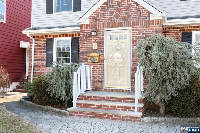 property entrance featuring brick siding and a shingled roof