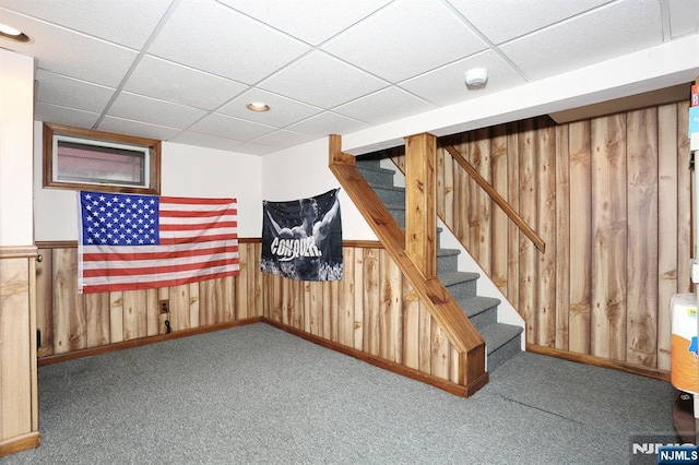 finished basement with carpet floors, a wainscoted wall, a paneled ceiling, stairway, and wood walls