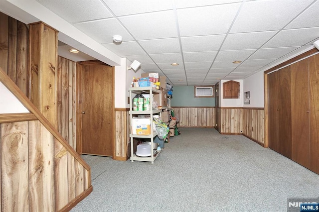 finished basement with a paneled ceiling, a wainscoted wall, carpet, and wooden walls