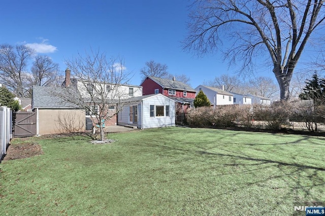 rear view of property with a lawn, a chimney, a gate, fence, and an outdoor structure