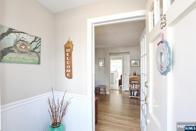 hall with light wood-style floors and a wainscoted wall