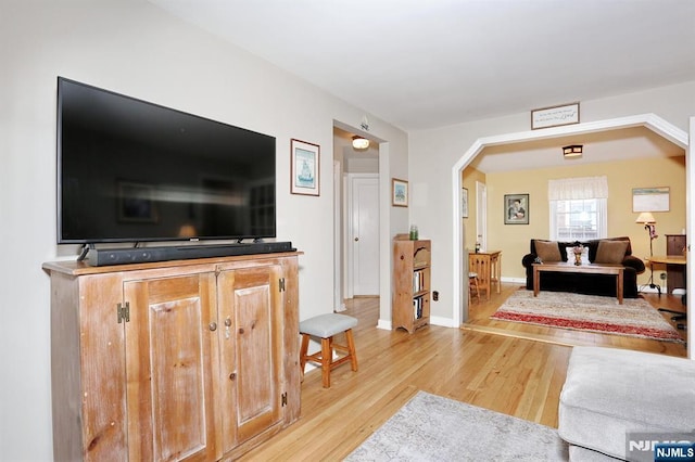 living area featuring light wood-type flooring, baseboards, and arched walkways