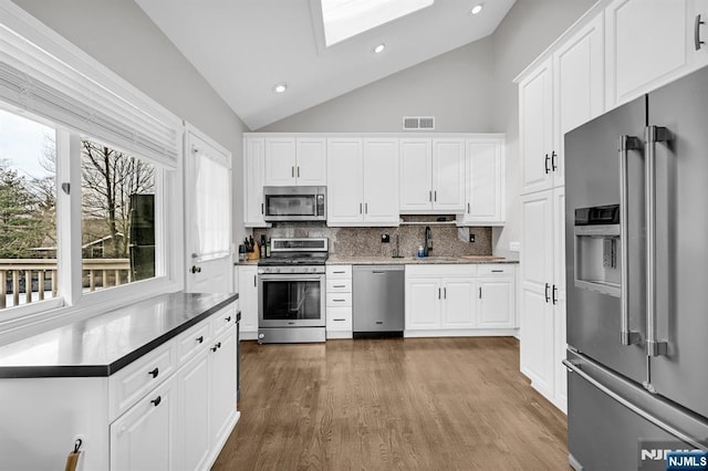 kitchen featuring a skylight, visible vents, decorative backsplash, stainless steel appliances, and a sink