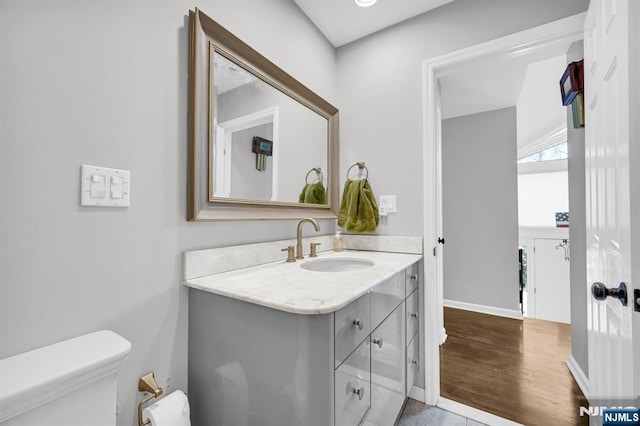 half bathroom featuring vanity, wood finished floors, toilet, and baseboards