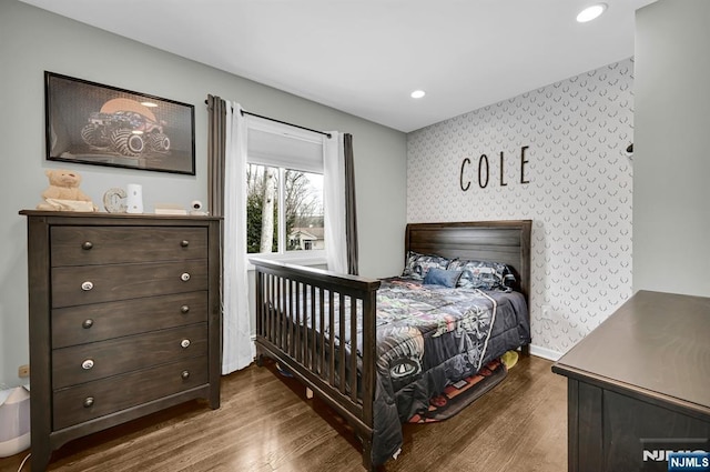 bedroom featuring an accent wall, dark wood finished floors, baseboards, and wallpapered walls