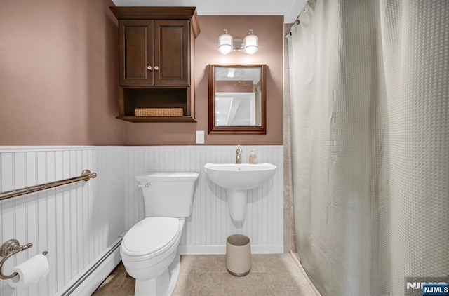 bathroom with curtained shower, toilet, a baseboard heating unit, wainscoting, and tile patterned floors