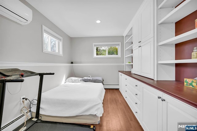 bedroom with baseboard heating, a wall mounted AC, a baseboard radiator, and light wood-style flooring