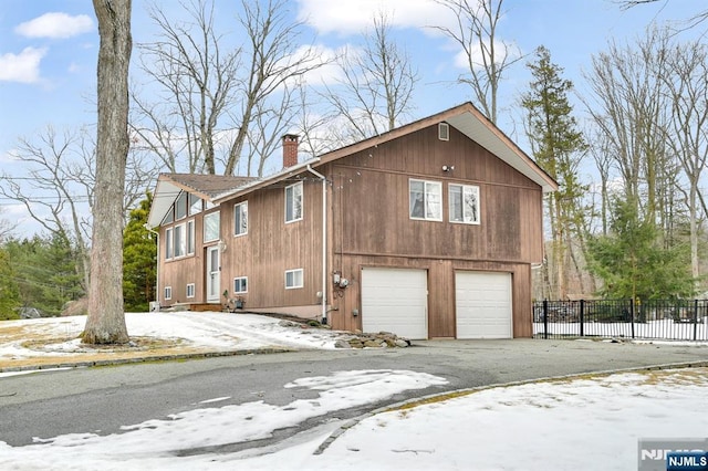 view of snow covered exterior with a garage, driveway, a chimney, and fence