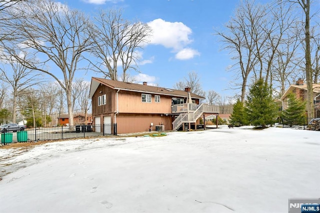 snow covered rear of property with a garage, stairs, fence, and a wooden deck