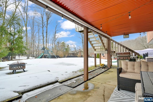 snow covered patio with a grill, stairs, fence, and a playground