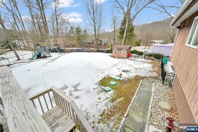 yard layered in snow with a storage unit, a playground, and an outbuilding