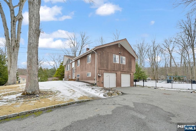 view of side of home with aphalt driveway, an attached garage, and fence