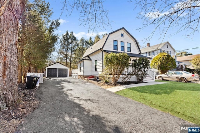 view of front of property featuring a garage, a front yard, an outbuilding, and a gambrel roof