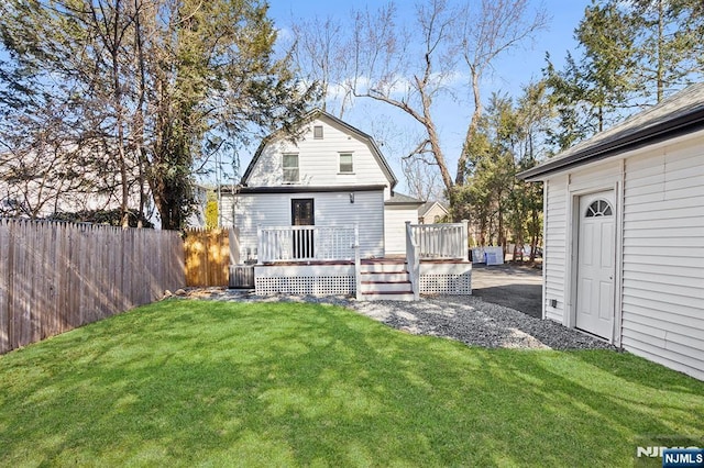 exterior space featuring a wooden deck, fence, a lawn, and a gambrel roof