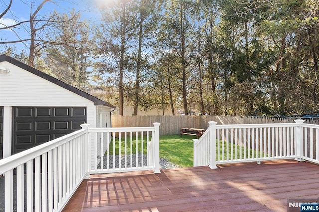 wooden terrace featuring a garage, a fenced backyard, and a lawn