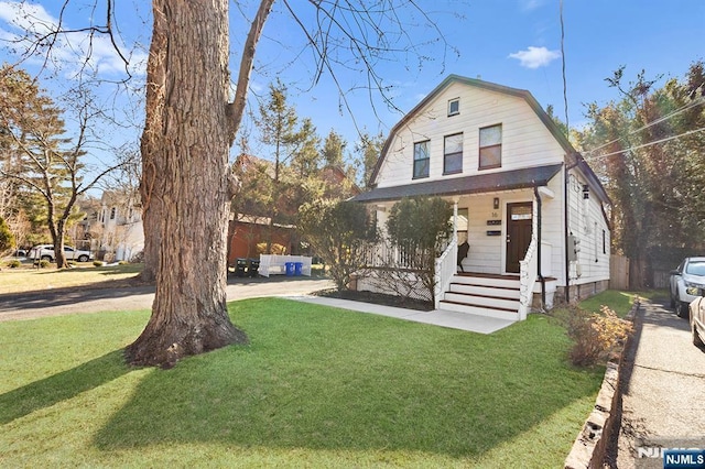 colonial inspired home with covered porch, a front yard, and a gambrel roof