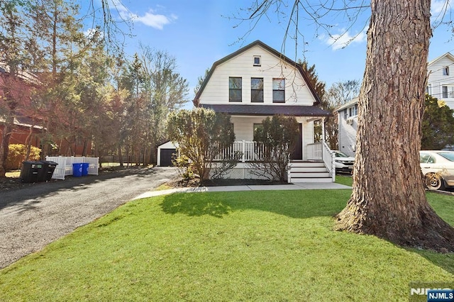 dutch colonial with a porch, a front lawn, a detached garage, and a gambrel roof