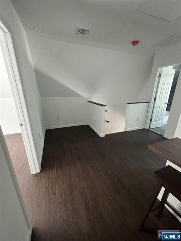 additional living space with vaulted ceiling, dark wood-style flooring, visible vents, and baseboards