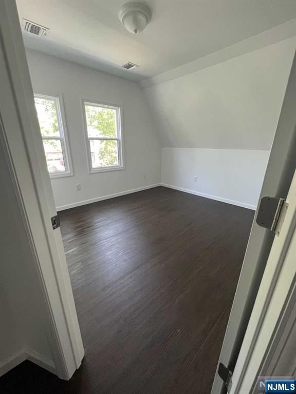 bonus room featuring baseboards, visible vents, vaulted ceiling, and dark wood-type flooring