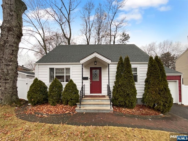 view of front of home with a garage, a shingled roof, and fence