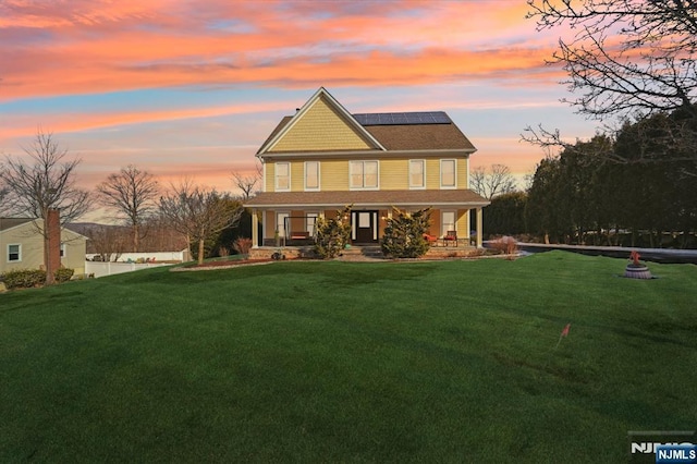 view of front of house with a porch, roof mounted solar panels, and a yard