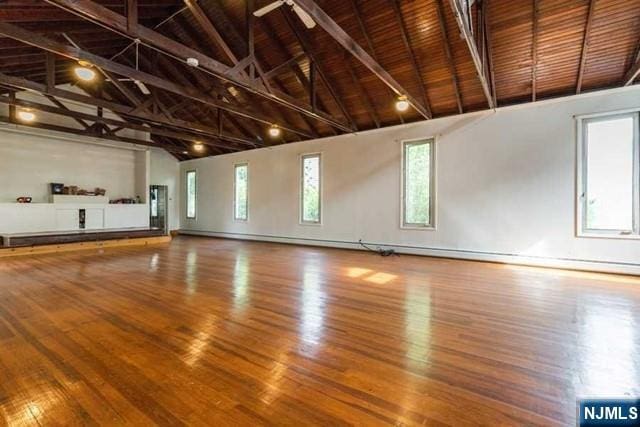 unfurnished living room with high vaulted ceiling, beamed ceiling, wood finished floors, and a healthy amount of sunlight