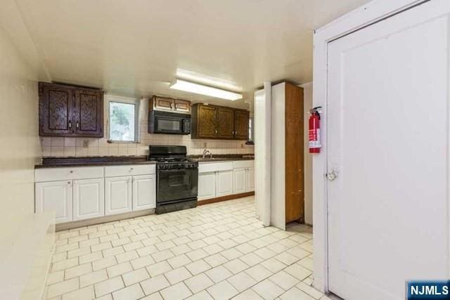 kitchen with decorative backsplash, dark countertops, black appliances, white cabinetry, and a sink