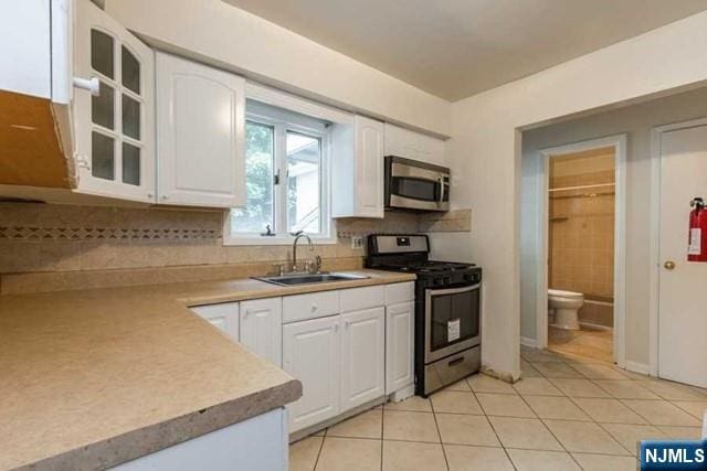 kitchen with light tile patterned floors, white cabinets, glass insert cabinets, stainless steel appliances, and a sink