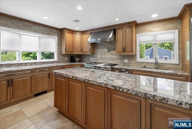 kitchen featuring brown cabinets, wall chimney range hood, a sink, and a healthy amount of sunlight