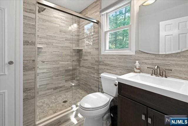 full bath with toilet, a stall shower, tile walls, and vanity