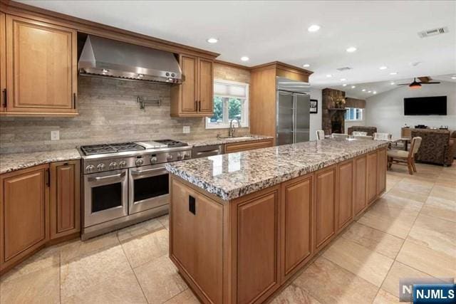 kitchen featuring light stone countertops, wall chimney range hood, a kitchen island, and premium appliances