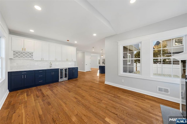 kitchen with blue cabinetry, tasteful backsplash, visible vents, wood finished floors, and beverage cooler