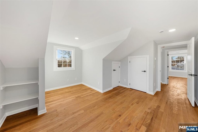 bonus room with baseboards, light wood-type flooring, lofted ceiling, and a healthy amount of sunlight