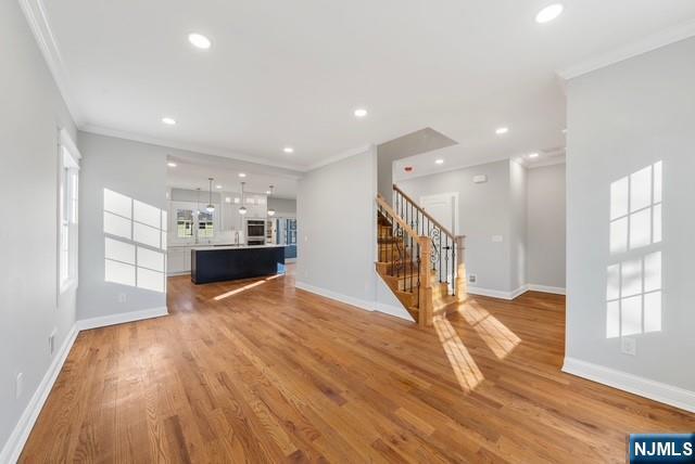 unfurnished living room with baseboards, stairs, crown molding, light wood-type flooring, and recessed lighting