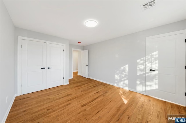 unfurnished bedroom featuring light wood-type flooring, a closet, visible vents, and baseboards