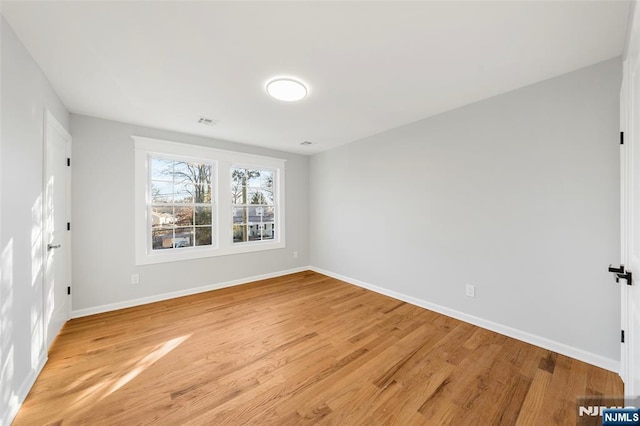 spare room with light wood finished floors, baseboards, and visible vents