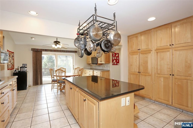 kitchen featuring light brown cabinetry, tasteful backsplash, stainless steel microwave, and a kitchen island