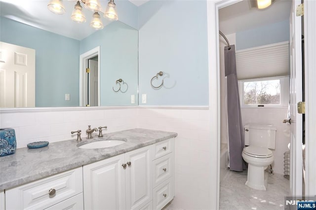 bathroom featuring toilet, a wainscoted wall, vanity, tile walls, and shower / bath combo with shower curtain