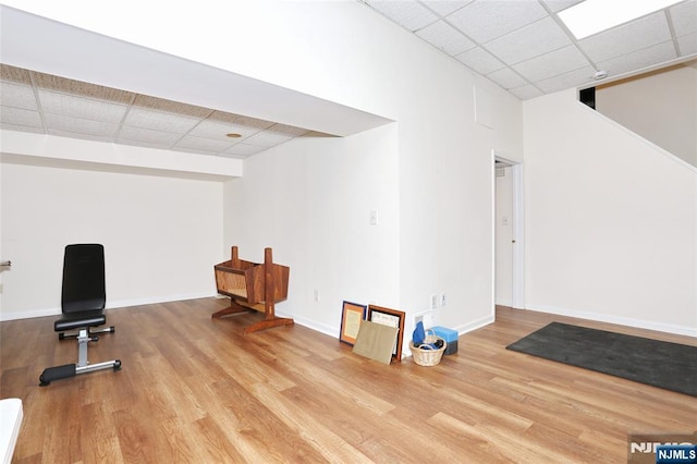 exercise room featuring baseboards, a drop ceiling, and wood finished floors