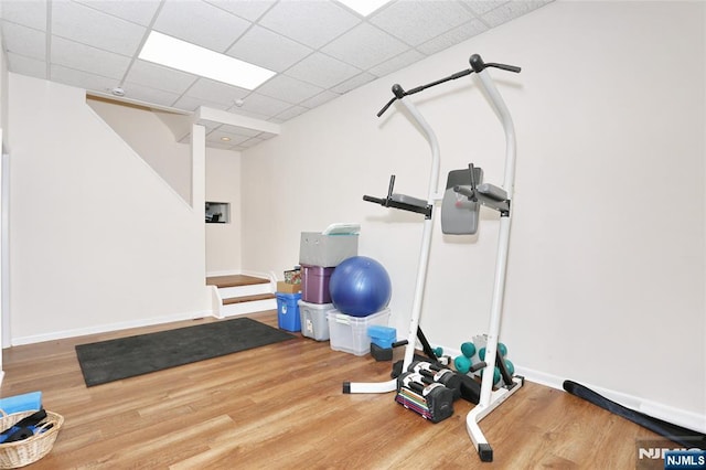 exercise room featuring a drop ceiling, baseboards, and wood finished floors