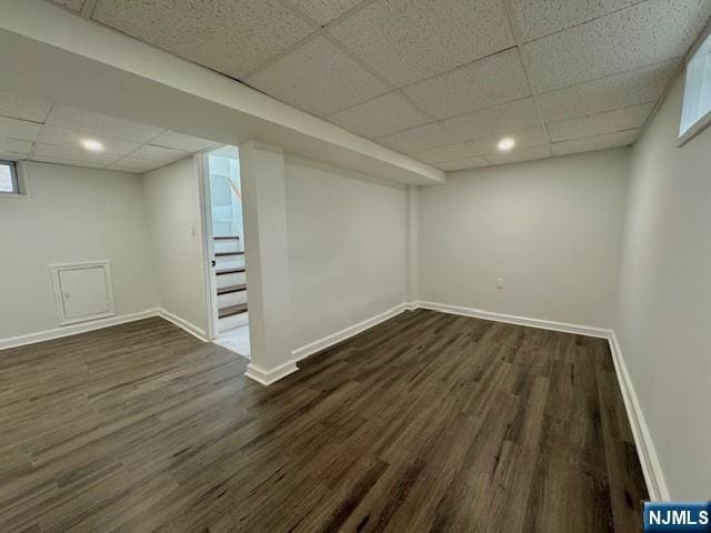 finished below grade area featuring baseboards, stairway, dark wood-style flooring, and a paneled ceiling