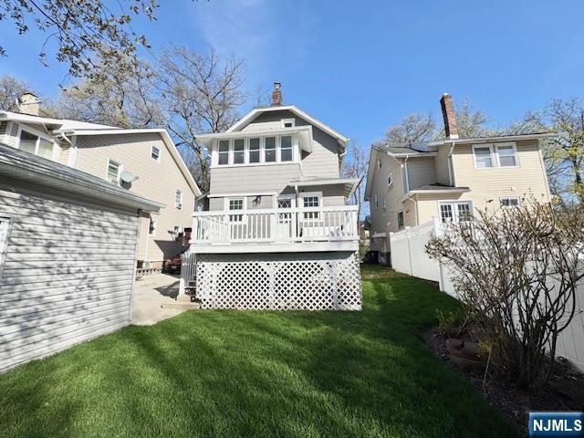 rear view of property featuring a lawn, fence, and a deck