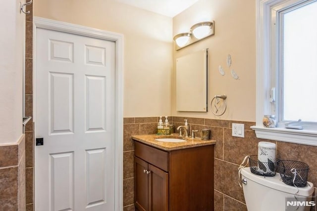 full bathroom with toilet, wainscoting, tile walls, and vanity