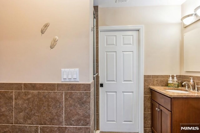 bathroom with a wainscoted wall, a tile shower, tile walls, and vanity