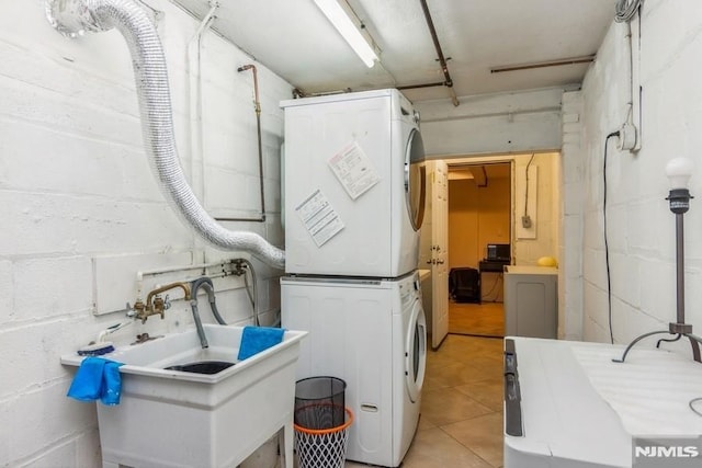 clothes washing area with concrete block wall, stacked washer and clothes dryer, a sink, and laundry area