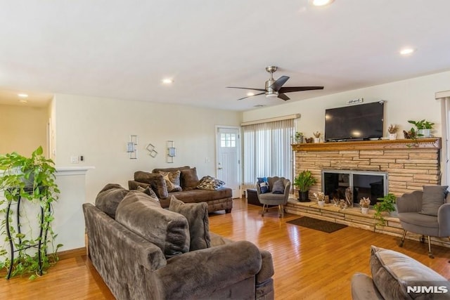 living room featuring recessed lighting, light wood-style flooring, a ceiling fan, and a stone fireplace