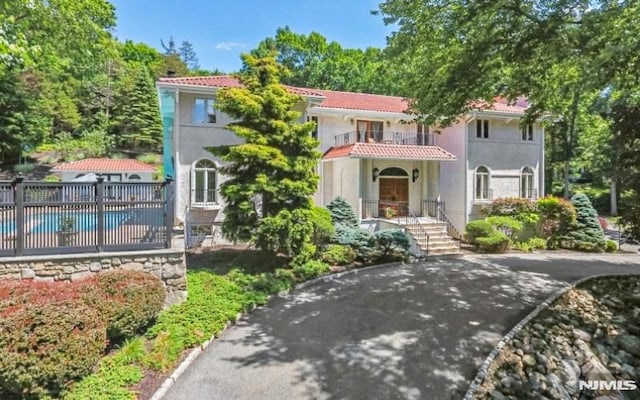 mediterranean / spanish home featuring a fenced in pool, fence, a tile roof, stucco siding, and a balcony